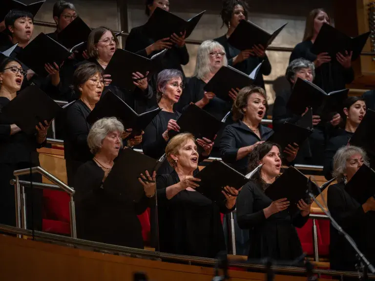 Photo depicts choir of women singing and holding up folders of sheet music