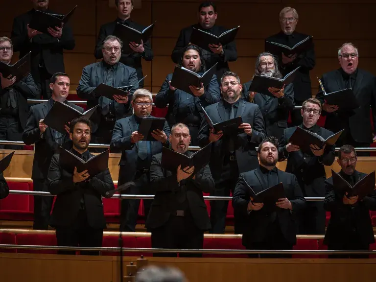 Photo depicts chorus of men singing from raised folders with sheet music