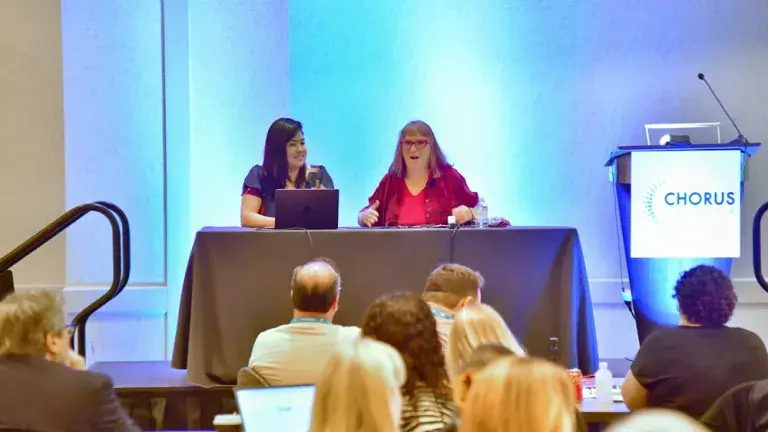 Photo depicts Maggie Vo and Beth Kanter seated side by side behind a table. They are on stage presenting to the audience in front of them