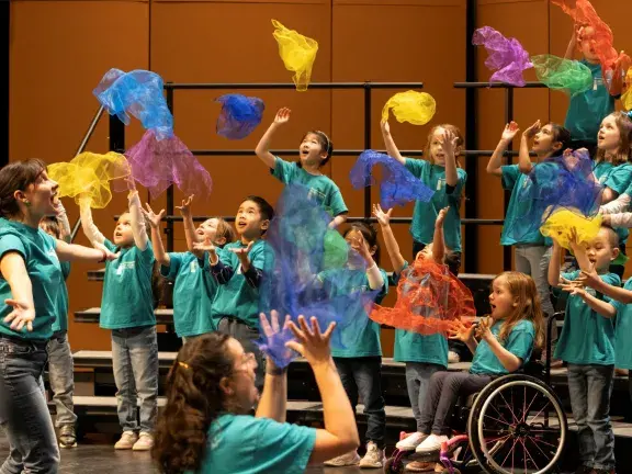 Children's choir on stage playing with multicolored scarves and throwing them in the air