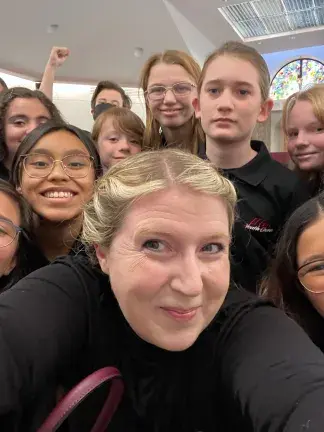 Chorus director and group of students posing for a photo.