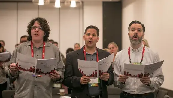 three men in a row holding sheet music and singing