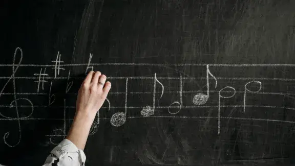 hand writing music notes on chalk board